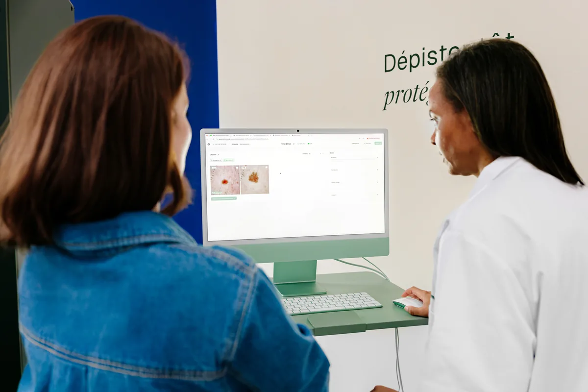 Consultation DermaScan : une patiente et une soignante analysent la cartographie des grains de beauté à l'écran.